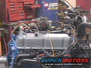 Engine block with blue paint, gray valve cover, and carburetor. Wires and hoses are connected