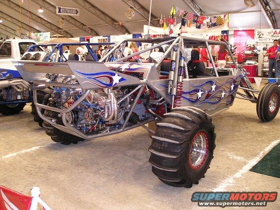 Silver sand rail buggy with red, white, and blue star graphics, exposed engine, and large paddle tires