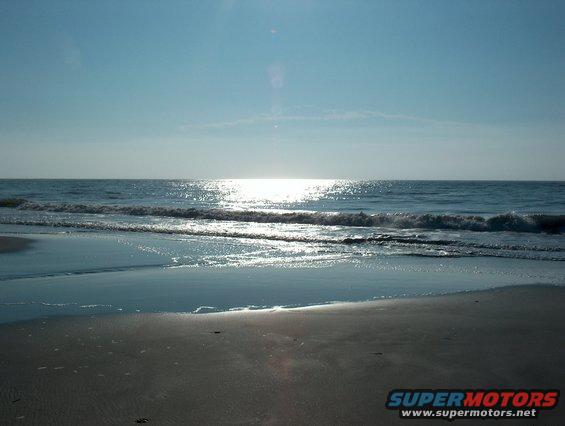 Ocean waves on a sandy beach with the sun reflecting on the water
