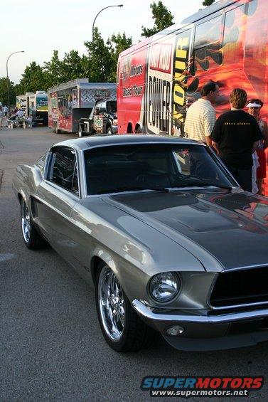 Silver classic Ford Mustang parked next to a large bus with graphics