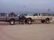 2000 Ford F-450 - Two lifted Ford trucks are parked on a sandy beach with a go-kart in the bed of one.