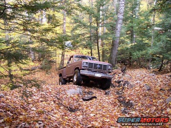 1980 Ford F-100 driving on a wooded trail covered in autumn leaves