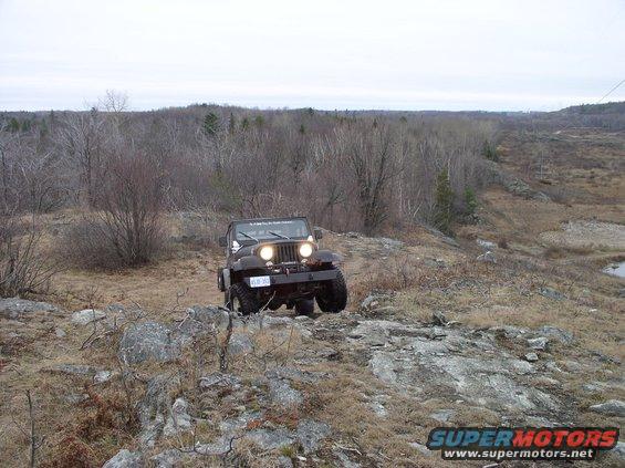 Black Jeep Wrangler on rocky terrain, front view with headlights on
