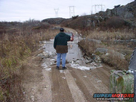 Red SUV navigating a water crossing on a rough dirt track