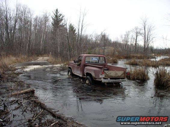 1980 Ford F-100 driving through icy water with trees in background