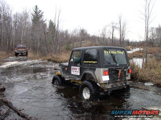 Jeep Wrangler driving through water with another truck behind it on a muddy trail