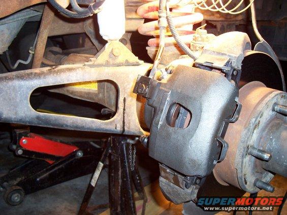 Close-up of a vehicle's brake caliper and suspension parts, with a jack and jack stand visible