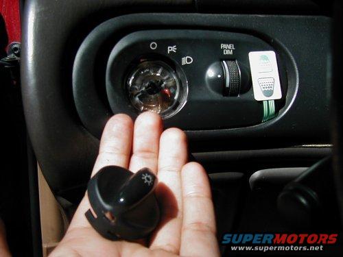 Hand holding light switch knob near dashboard panel dimmer and headlight controls
