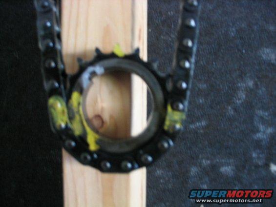 Close-up of a timing chain and sprocket held by a wooden block