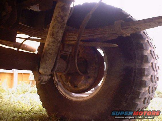 Close-up of a vehicle's rear tire and suspension system, showing leaf springs and a shock absorber