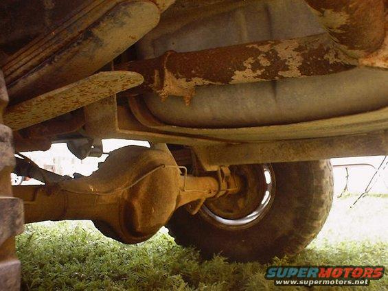 Undercarriage of a rusty vehicle, showing leaf springs, differential, exhaust pipe, and tire