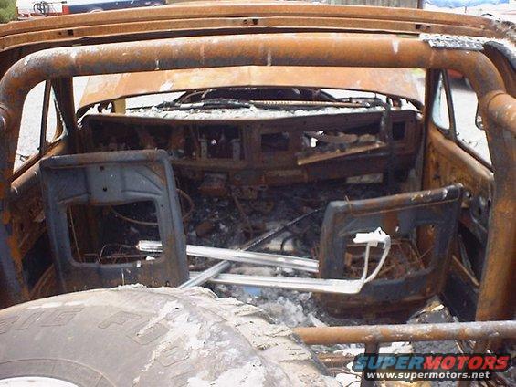 Burnt-out interior of a 1978 Ford Bronco with a roll cage, showing melted dashboard and seats