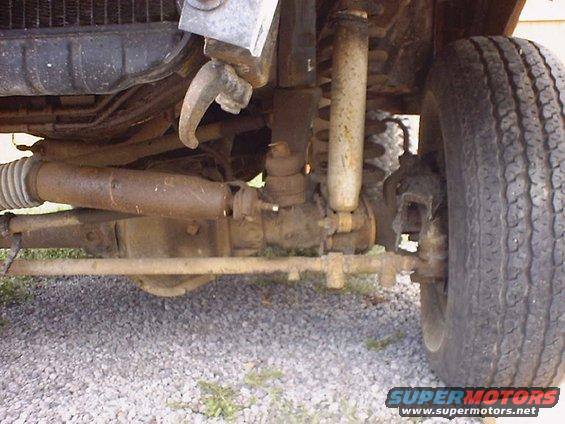 Close-up of rusty front axle, steering linkage, shock absorber, and tire of a vehicle
