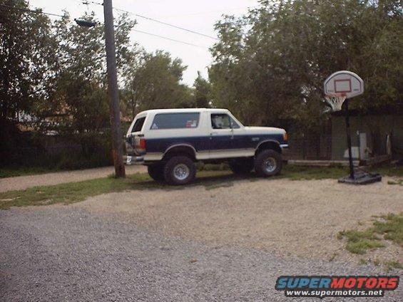 Lifted blue and white Ford Bronco parked outside next to a basketball hoop