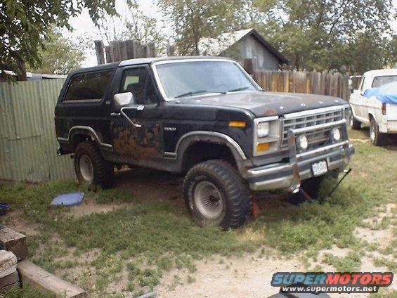 Black Ford Bronco with rust damage, parked on grass. Front grille and headlights visible