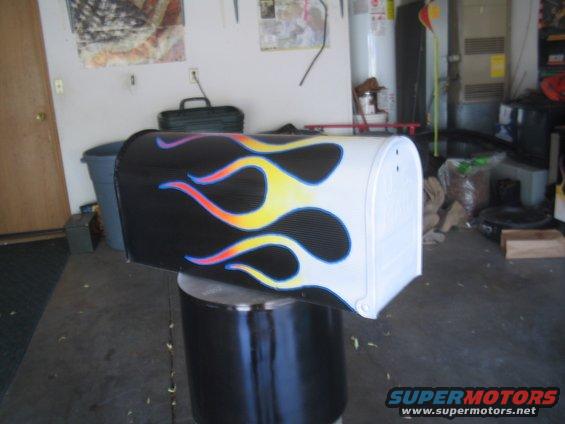 Black and white mailbox with yellow, orange, and purple flame graphics, displayed on a black cylindrical stand