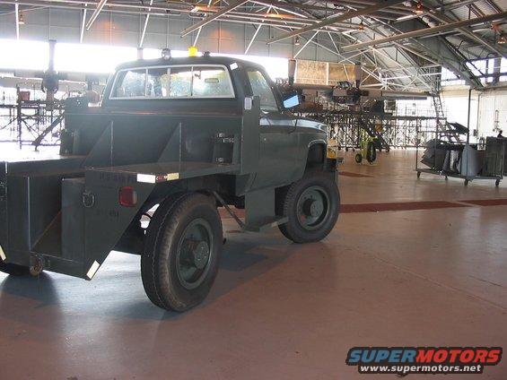 Green utility truck with a flatbed and toolboxes parked inside a large building