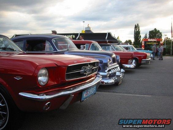 Red classic Mustang in front, followed by a blue sedan and other vintage cars parked outside a McDonald's