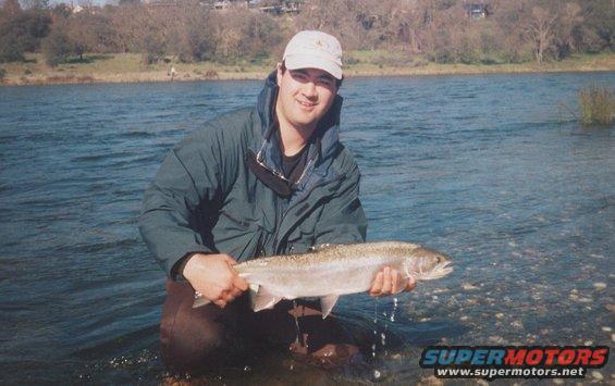 Man in waders and jacket holding a large fish in a river