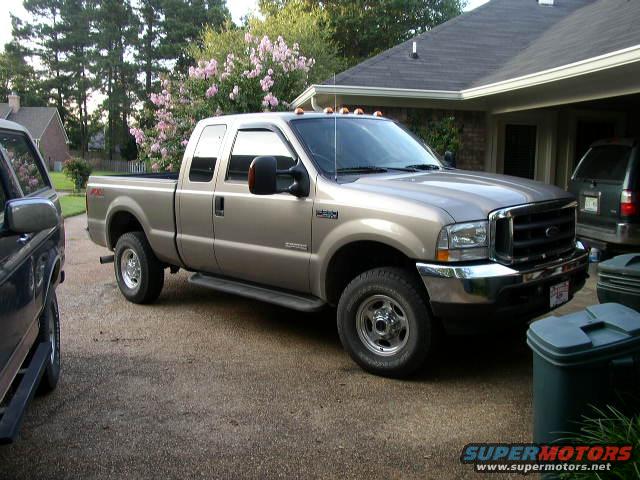 Tan Ford F-250 Super Duty pickup truck parked in driveway next to a dark SUV