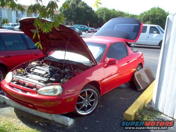 Red Mazda MX-3 coupe with hood and trunk open, parked on asphalt