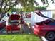1992 Ford Probe - Two people are working on the engine of a red coupe while another red coupe sits nearby with its trunk open.