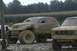 1989 Ford Bronco - Two off-road vehicles are covered in mud, parked next to a cornfield.