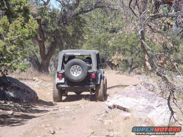 Jeep Wrangler with spare tire on rear, driving on a dirt road