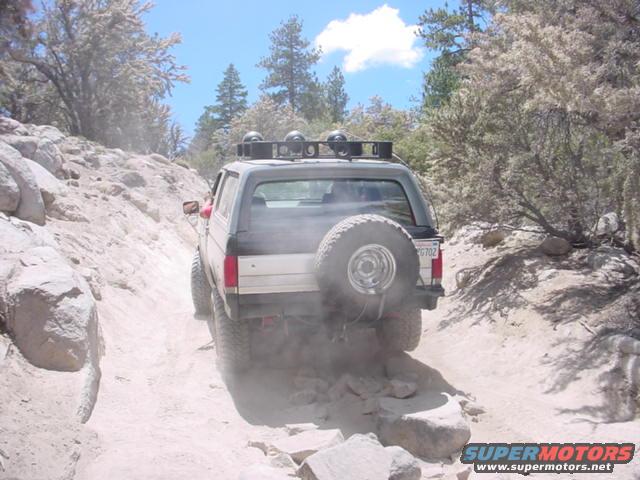 Rear view of a 1987 Ford Bronco driving on a dusty, rocky trail
