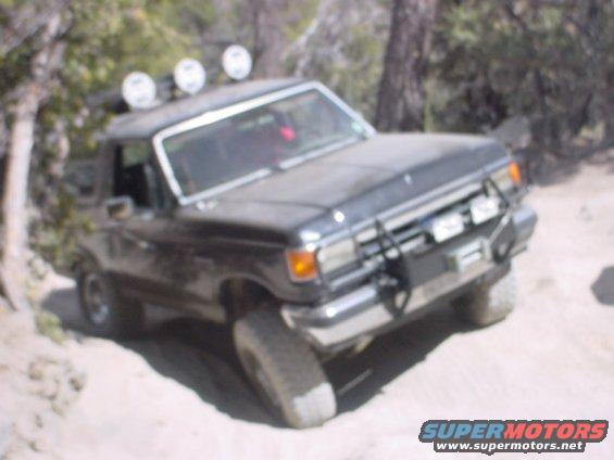 Dark SUV with off-road lights on roof, driving on a dirt path