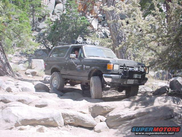 Dark Ford Bronco driving over rocks on a trail, driver visible