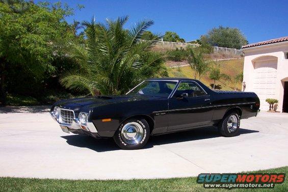 Black 1972 Ford Ranchero parked on a driveway with palm trees and a house in the background