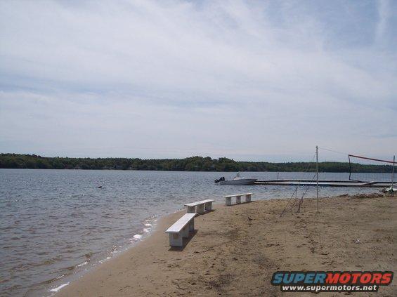 White boat docked on a lake with a sandy beach and benches