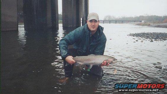 Man in waders holding a large fish in a river under a bridge