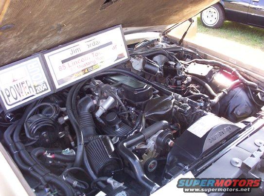 Engine bay with a sign that reads 'Jim Jordan 85 Lincoln Town Car Mustang GT Over 450,000 Miles POWER 2004'