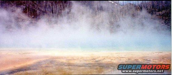 Geothermal area with steam rising from colorful ground and trees in background. Supermotors.net logo visible