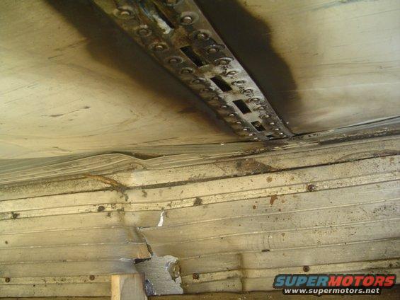 Damaged trailer interior with bent metal and water stains. A metal strip with rivets runs across the top