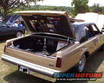 Gold 1985 Lincoln Town Car with trunk open, showing stickers and a trophy inside