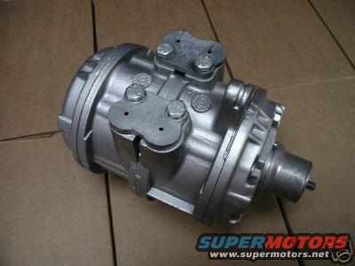 Silver metal automotive part with bolts and mounting brackets against a cardboard background