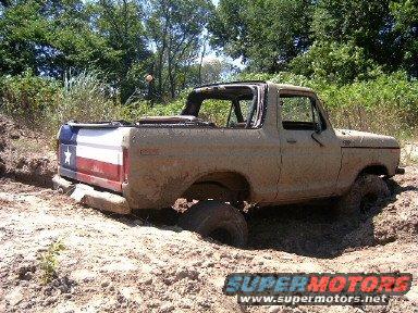 Tan 1978 Ford Bronco with Texas flag tailgate stuck in mud