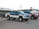 1994 Ford Bronco - Two custom lifted pickup trucks are parked side-by-side, with the truck in the foreground a white and blue paint scheme and custom decals.