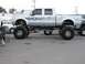 1994 Ford Bronco - A heavily modified silver pickup truck with custom flame decals and massive tires is parked outdoors.