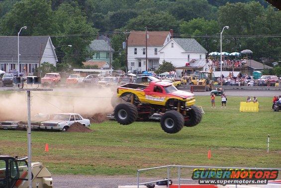 Monster truck mid-air over crushed cars, spectators in background