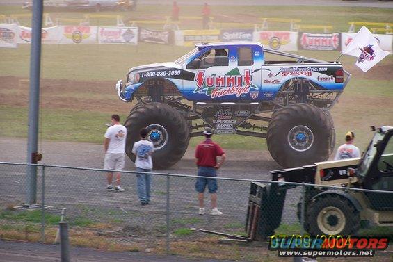 Monster truck with blue and white paint, large tires, and "Summit Truck Style" graphics