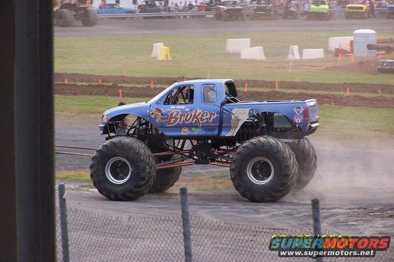 Blue monster truck with large tires and "Broker" text on its side, seen from the side