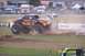 1979 Ford Bronco - A monster truck with flame graphics kicks up dirt as it drives across a track, with other vehicles blurred in the background.