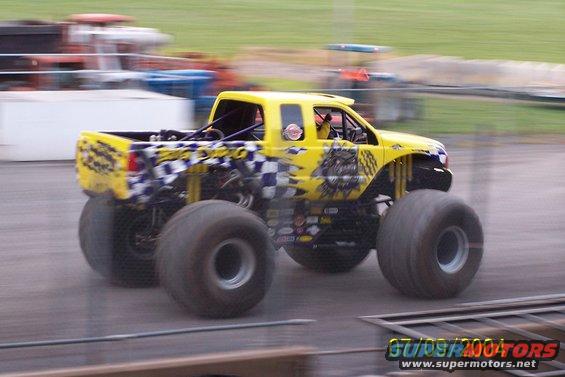 Yellow monster truck with checkered flag graphics and large tires, in motion