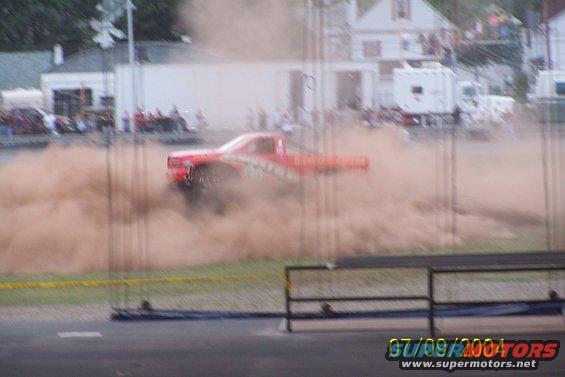 Red pickup truck in side view, kicking up a large dust cloud
