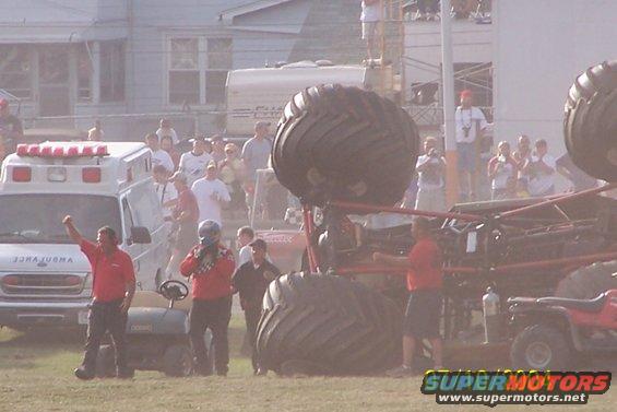 Monster truck with large tires and red frame, an ambulance, and ATVs on a dirt field