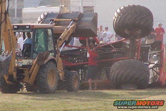 Backhoe lifting a monster truck with large tires